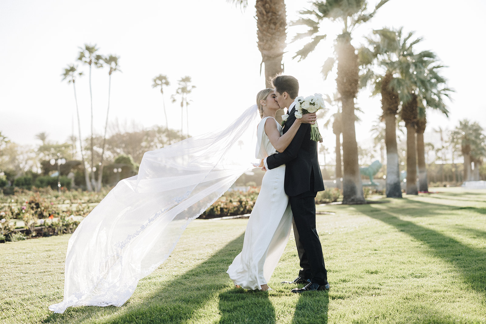 a female with blonde hair and a white wedding gown with her groom in an all black tux at their Coachella valley wedding