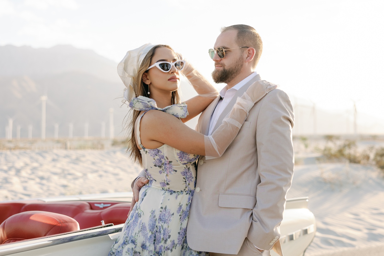 woman wearing a white with blue florals dress and man in a tan linen suit posing for their California engagement photos